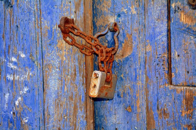 Rusty padlock and chain on a weathered blue wooden door