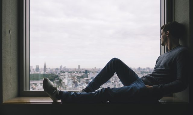 Man sitting by a window looking out over the city in a reflective moment