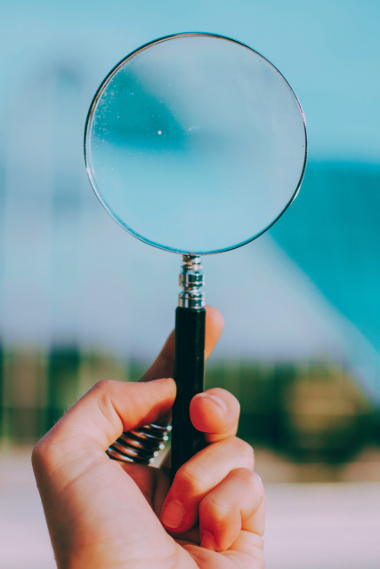 Hand holding a magnifying glass distorting the background, representing how language can amplify or alter meaning